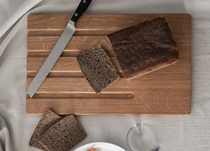 Brotschneidebrett "Falke" aus Eichenholz mit breiten Krümelrillen, darauf frisch geschnittenes Roggenbrot, ideal zum sauberen Schneiden und Servieren von Brot.